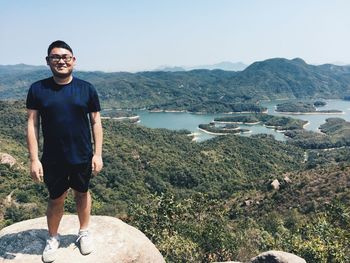 Portrait of young man standing on mountain against sky