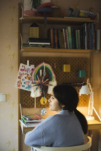 Rear view of thoughtful girl sitting at desk during studies at home