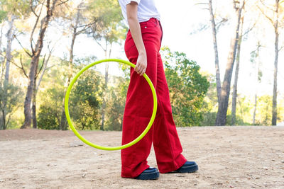 Side view of crop unrecognizable female teen in red jeans holding hula hoop while having free time in park