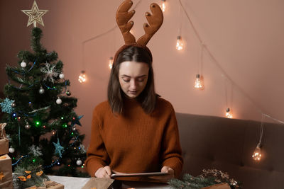 Portrait of young woman standing by christmas tree at home