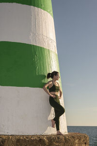 Fit sporty woman resting after exercise, leaning against a lighthouse.