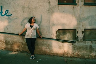 Young woman looking away while standing against wall