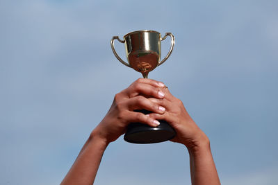 Cropped hands of woman holding trophy against sky