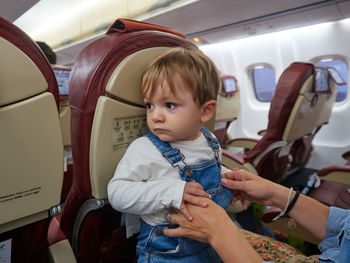 Crop mother playing with adorable toddler while sitting on passenger seat on board of airplane