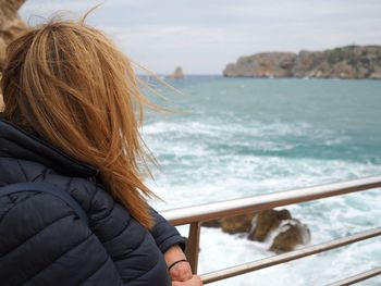 Woman in warm cloths looking at sea against sky