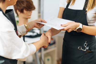 Hands of hairdressing educator giving hairstylist certificate to a student 