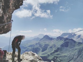 Man standing on cliff by mountains against sky