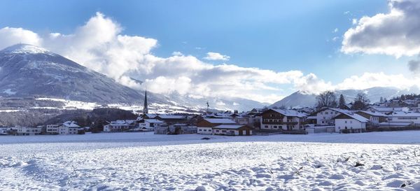 Snow covered houses by buildings against sky