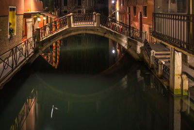 Footbridge over canal amidst buildings at night