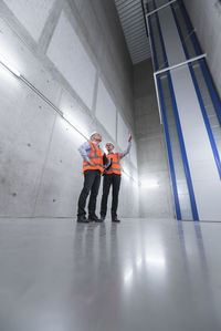 Two colleagues wearing safety vests and hard hats talking in a building