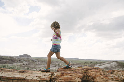 Side view of girl walking on rocks against cloudy sky