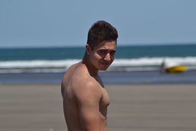 Portrait of shirtless man standing at beach against sky