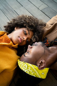 Top view of trendy african american man and woman in bright coat lying opposite with face to face looking at each other