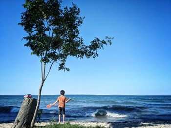 Man standing by sea against clear blue sky