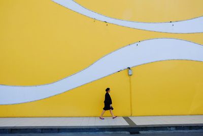 Side view of people walking on yellow wall