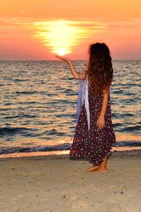 Rear view of woman standing on beach during sunset