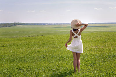 Rear view of woman with arms raised standing on grassy field against sky