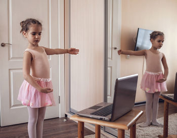 Pretty young ballerina practicing classic choreography during online class, social distance