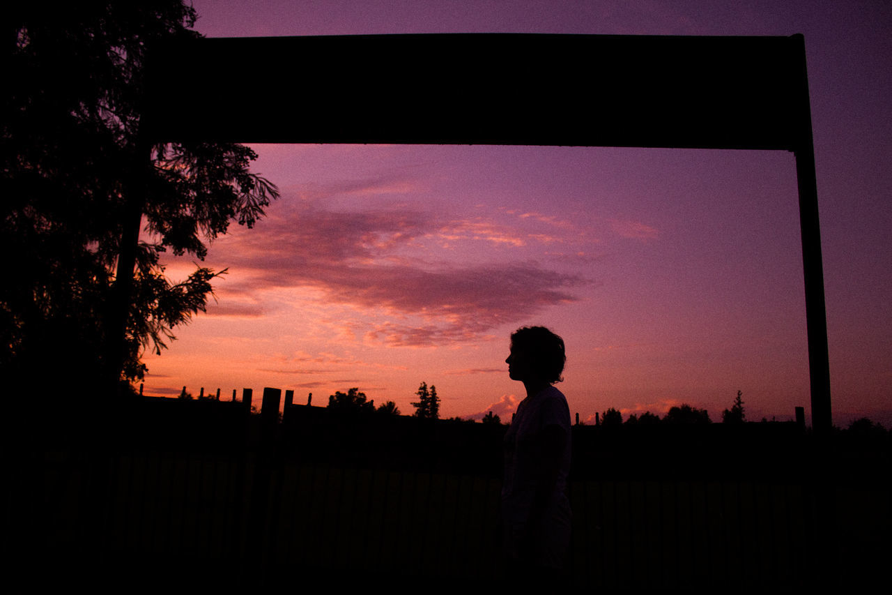 SILHOUETTE MAN STANDING BY TREE ON FIELD AGAINST SKY AT SUNSET