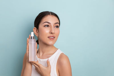 Portrait of young woman holding thermometer against blue background