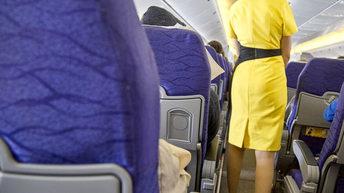 Midsection of air hostess wearing yellow uniform working in airplane