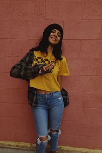 Portrait of smiling young woman standing against wall