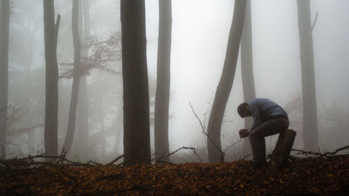 Side view of depressed man sitting on tree stump in forest during foggy weather