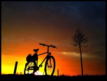 Silhouette of bicycle on field against sky during sunset