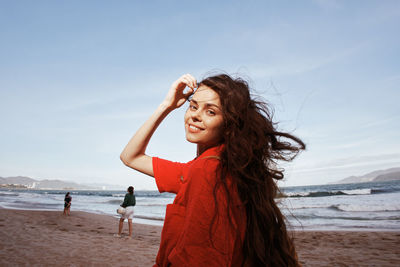 Young woman standing at beach against sky