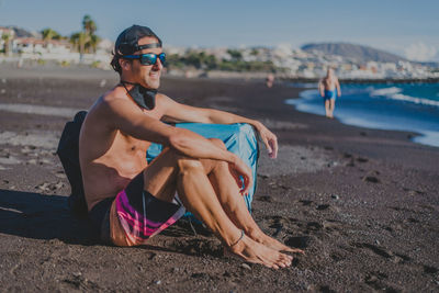 Young man in cap and glasses and surf clothes looks at the sea with mask corona