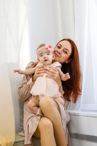 Smiling young mother is holding her little daughter in hands. candid family portrait.