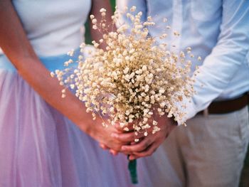 Midsection of wedding couple holding white flowers