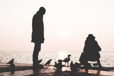 Silhouette people at beach against sky during sunset