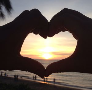 Silhouette hands forming heart shape against sky during sunset