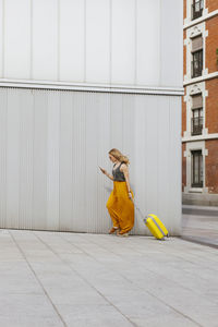 Full length of woman with luggage walking by wall