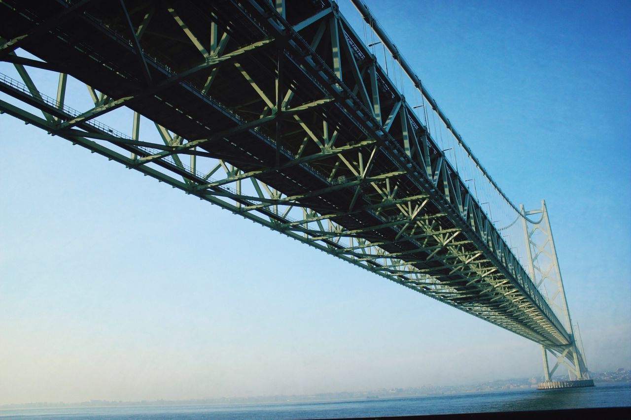 connection, clear sky, engineering, low angle view, suspension bridge, built structure, bridge - man made structure, water, blue, sea, transportation, architecture, bridge, sky, copy space, cable, outdoors, no people, metal, day