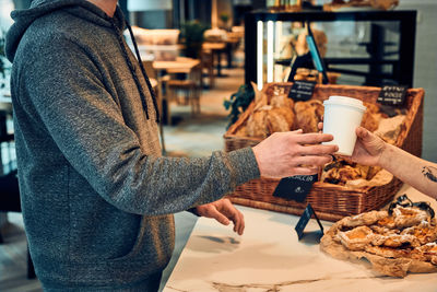 Man buying coffee and pastry in the coffee shop to go. man taking coffee cup from barista