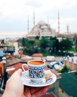 Cropped hand holding tea cup against sultan ahmed mosque in city