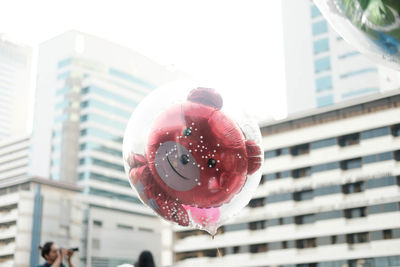 Low angle view of balloon holding umbrella against buildings in city