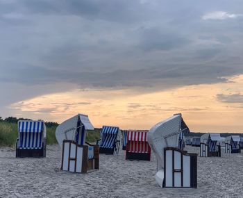 Hooded chairs on beach against sky during sunset