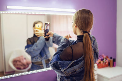 Rear view of woman taking selfie with smart phone while looking in mirror