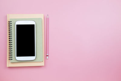 High angle view of smart phone with books and pencil over pink background