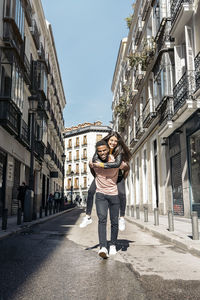 Full length of man carrying woman on back amidst buildings