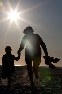 Silhouette of mother and daughter running at beach during sunset