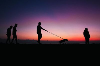 Silhouette men on field against orange sky