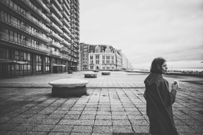 Side view of woman standing on footpath in city