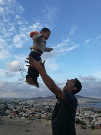 Father catching boy against sky