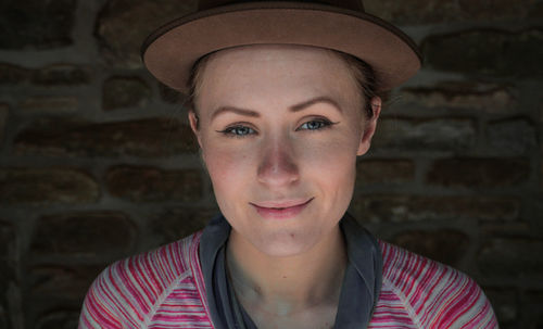 Close-up portrait of woman in hat against brick wall