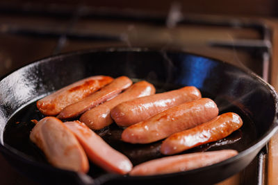Half-cut sausages are fried in oil in a black cast-iron skillet