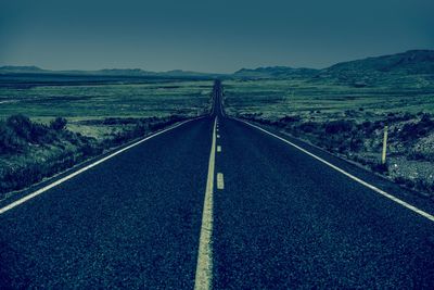 Road leading towards mountains against clear sky